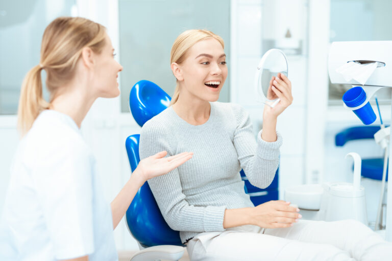 A woman is sitting at a dentist's reception. She looks in the mirror at her teeth. Woman smiling